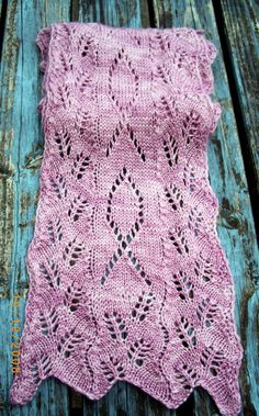 a pink crocheted blanket sitting on top of a wooden table next to a piece of wood