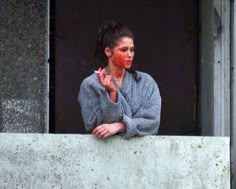 a woman with red paint on her face and hands standing in front of a window