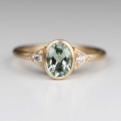 Oval Multi Stone Engagement Ring, Green Sapphire Bezel Ring, Pale Green Engagement Ring, 14k Gold Three-stone Oval Ring, Modern Oval Emerald Ring With Accent Stones, Oval Three Stone 14k Gold Ring, Three Stone Oval 14k Gold Ring, Art Deco Sapphire Ring In 14k Gold, Art Deco Oval Sapphire Ring In 14k Gold