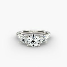 three stone engagement ring with side stones in white gold, set on a plain surface