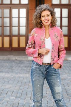 a woman standing in front of a building wearing ripped jeans and a pink cardigan