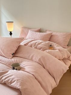 an unmade bed with pink sheets and pillows on top of it, next to a lamp