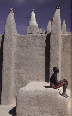 a person sitting on a rock in front of some concrete structures with birds flying overhead