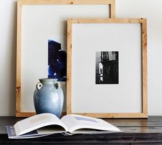 an open book sitting on top of a wooden table next to a vase and framed photograph