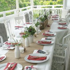 a long table set with place settings for dinner on a porch overlooking the trees and bushes