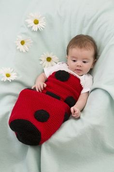 a baby laying on top of a bed with a crochet ladybug blanket