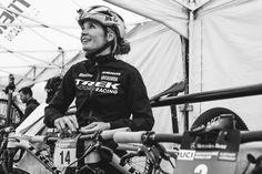 black and white photograph of a woman with her bike in front of a tented area