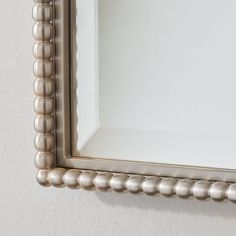 a silver framed mirror hanging on the wall with beaded trim around it's edges