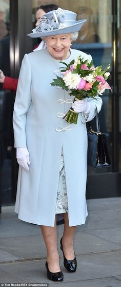 an older woman in a blue coat and hat with flowers on her lap is walking down the street