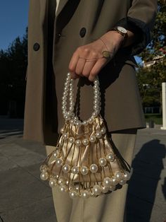 Elevate your style with our exquisite bridal clutch bag, crafted for both brides and guests attending special events. The luxurious mink color satin provides a sophisticated backdrop, complemented by large white pearls that encircle the bag, creating an opulent and timeless look. The handle, adorned with white pearls, adds a touch of glamour and refinement. Whether you're walking down the aisle or attending a special event, this clutch is designed to make a statement. The meticulous craftsmanship, coupled with the use of yellow threads, adds a subtle warmth, making it versatile for both daily and wedding occasions. Key Features: Luxurious mink color satin White pearl handle for a touch of elegance Large white pearls embellish the bag Versatile for daily and wedding events Meticulous crafts Elegant Pouch Clutch With Pearl Handle, Cream Clutch Evening Bag For Party, Pearl Handle Clutch For Wedding Guests, Cream Handheld Clutch For Party, Gold Bag With Pearl Handle For Events, Beige Clutch With Pearl Handle For Event, Beige Clutch With Pearl Handle For Events, Chic Wedding Clutch With Pearl Handle, Elegant Handheld Bags For Wedding Guest