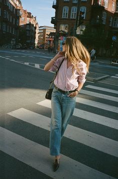 a woman is walking across the street talking on her cell phone while wearing jeans and heels