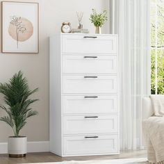 a white chest of drawers next to a window in a room with a potted plant