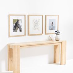 three framed pictures hang on the wall above a wooden bench with vases and flowers