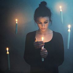 a woman holding a lit candle in front of her face and looking down at it