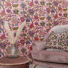 a pink chair sitting in front of a wall covered with flowers and feathers on it