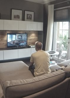 a man sitting on top of a couch in front of a tv mounted to a wall