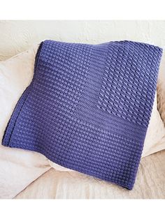 a blue knitted pillow sitting on top of a bed next to a white pillow