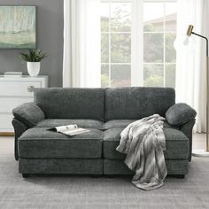 a living room scene with focus on the grey couch and throw blanket that's folded over it