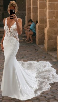 a woman in a white wedding dress taking a selfie with her cell phone while standing outside