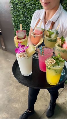 a woman sitting at a table with many drinks on top of it and holding a drink in her hand