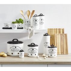 the kitchen is decorated in white and has black pots with lids on them, along with wooden utensils