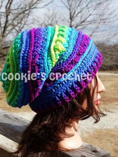 a woman wearing a multicolored crocheted hat on top of a wooden bench