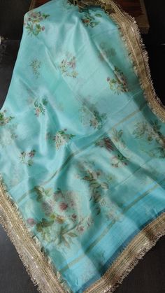 Make a stunning statement with this Teal Pure Organza Silk Saree, beautifully adorned with a vibrant floral digital print that captures the essence of nature. The lightweight organza fabric offers a delicate drape, creating an airy and ethereal silhouette that enhances your elegance. The floral patterns, bursting with rich colors, bring a lively charm to the saree, while the intricate lace trim border adds a touch of sophistication and refinement. Ideal for various occasions, from casual gatherings to festive celebrations, this saree effortlessly combines style and comfort. With its captivating design and luxurious feel, this teal saree is sure to make you stand out in any crowd. Designer Blue Floral Print Dupatta, Festive Silk Saree With Floral Print, Festive Floral Print Silk Saree, Summer Designer Silk Dupatta, Elegant Blue Dupatta With Digital Print, Spring Floral Print Saree, Summer Digital Print Saree, Bohemian Organza Dupatta For Designer Wear, Silk Chiffon Unstitched Wedding Dupatta