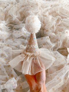 a hand is holding a small white cone top hat with sequins on it