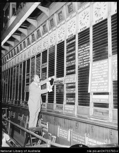 an old black and white photo of a man writing on a wall with many clocks