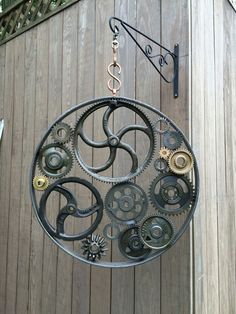 a metal clock hanging from the side of a wooden building with gears attached to it