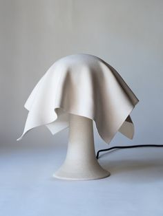 a white table lamp with a black cord on it's end and an object in the background