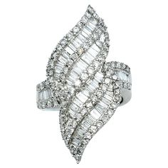 Ring size: 7.5 This lustrous, sparkling cocktail ring is a captivating embodiment of modern artistry and timeless luxury. Crafted in shimmering 14 karat white gold, its design is a marvel, resembling fiery flames that dance with movement. This distinctive ornament is adorned with a mesmerizing array of baguette and round diamonds, which, in unison, create an intricate play of light and shadow. The elegant piece absolutely glows, drawing all eyes to the hand and flattering the finger with its elongated silhouette. The diamonds, both round and baguette-cut, continue their scintillating journey along the shank of the ring, ensuring that elegant shimmer and sparkle grace every facet of this opulent creation. The high polish of the white gold adds more reflective glimmer to this piece, further Sparkling Cocktail, Timeless Luxury, All Eyes, Fine Jewelry Collection, Brilliant Diamond, All About Eyes, Diamond Clarity, Cocktail Ring, Light And Shadow