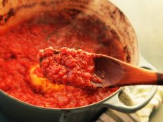 a wooden spoon full of red sauce on top of a pot filled with tomato sauce