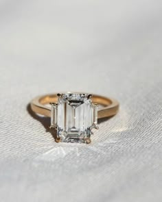 an emerald - cut diamond ring sits on a white cloth