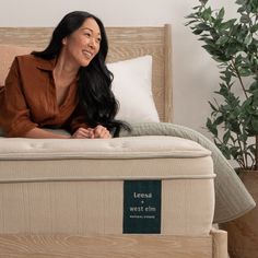 a woman laying on top of a bed next to a potted plant and pillows