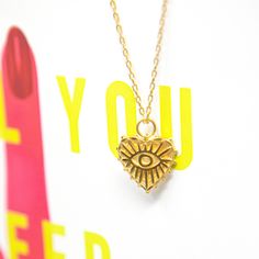 A lovely gold heart pendant with an evil eye design in the center of the heart! We love this gold style - show your love and ward off evil! This classic pendant style is easy to pair with any other TSK necklaces. We love this with the flat gold choker. Details: Material: High quality gold plated brass Style: Pendant 15" chain with 2" extension, spring clasp Pendant measures 3/4" diameter Trendy Gold Heart Charm Necklaces, Trendy Gold Heart Charm Necklace, Gold Heart Evil Eye Jewelry, Heart-shaped Gold Evil Eye Jewelry, Gold Heart-shaped Evil Eye Jewelry, Gold Jewelry With Heart Graphic For Valentine's Day, Symbolic Gold Heart-shaped Necklaces, Eye Pendant Necklace, Gold Heart Pendant