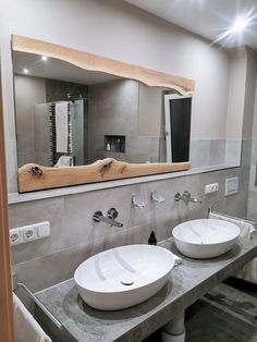 two white bowls are on the counter in front of a large mirror that is mounted to the wall