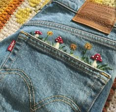 a pair of jeans with embroidered flowers and mushrooms on the back, sitting on a rug