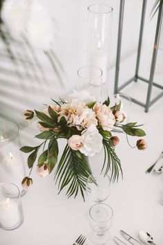 a vase with flowers and greenery sits on a table next to silver cutlers