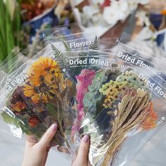 a person holding flowers in their hands with clear bags over them that say dried wildflowers