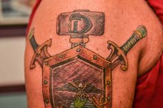 a man with a tattoo on his arm has a shield and two swords in front of him