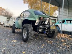 an old green car parked in front of a garage