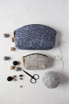 two small purses sitting on top of a table next to yarn, scissors and balls of thread