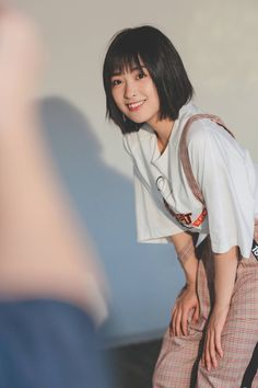 a woman with short black hair is sitting on a bed and smiling at someone in the mirror