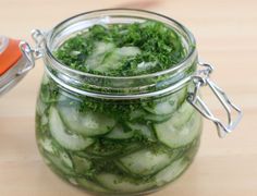 a glass jar filled with cucumbers on top of a wooden table next to an orange knife