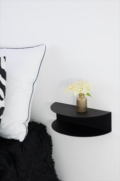 a vase with flowers on a black shelf next to a white wall and a pillow