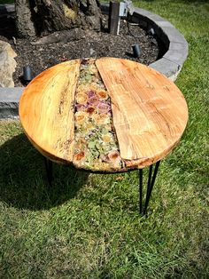 a wooden table sitting on top of a lush green field next to a fire pit