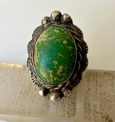 a pretty spectacular old ring, large, with a wonderful green turquoise.  i am a huge fan of these old pieces of turquoise, and this ring, for that matter.  it's beautifully crafted with lots of detail and a scalloped edge.  it has some wear, both on the silver and the stone, but basically nice condition.  unmarked sterling. size:  7 height of face:  1 and 5/16" width of inner band:  3/16" Southwestern Green Turquoise Ring With Large Stone, Southwestern Style Green Turquoise Ring With Large Stone, Southwestern Green Ring With Large Stone, Southwestern Style Green Turquoise Ring As Gift, Southwestern Green Cabochon Rings, Bohemian Green Chrysoprase Ring, Collectible Green Patina Jewelry, Green Untreated Collectible Jewelry, Vintage Green Turquoise Cabochon Ring