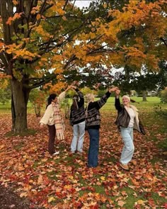 three women standing under a tree with their arms in the air and leaves on the ground