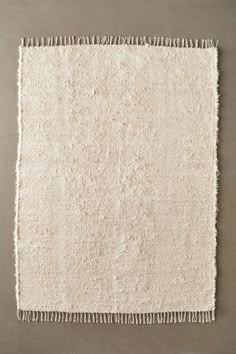 a white rug with fringes on the bottom and sides, in front of a gray wall